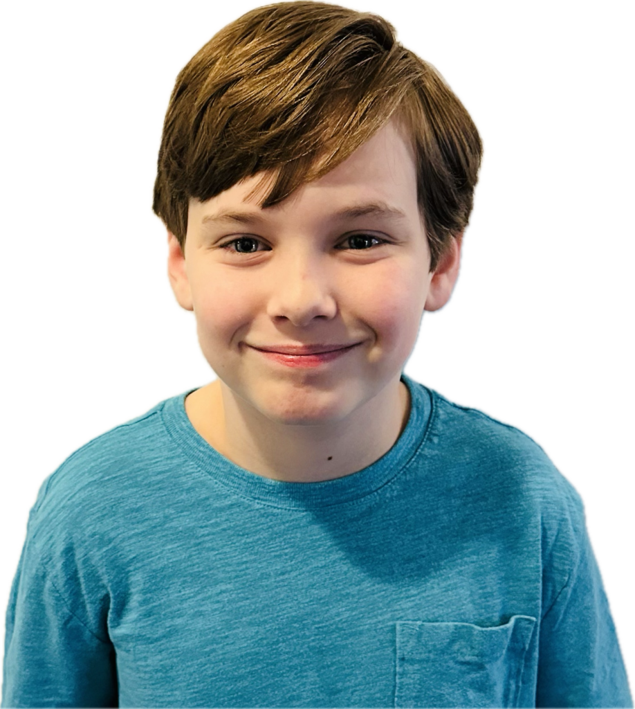 A young boy with short brown hair is smiling gently. He is wearing a blue t-shirt. The background is plain, emphasizing the boy's friendly expression.